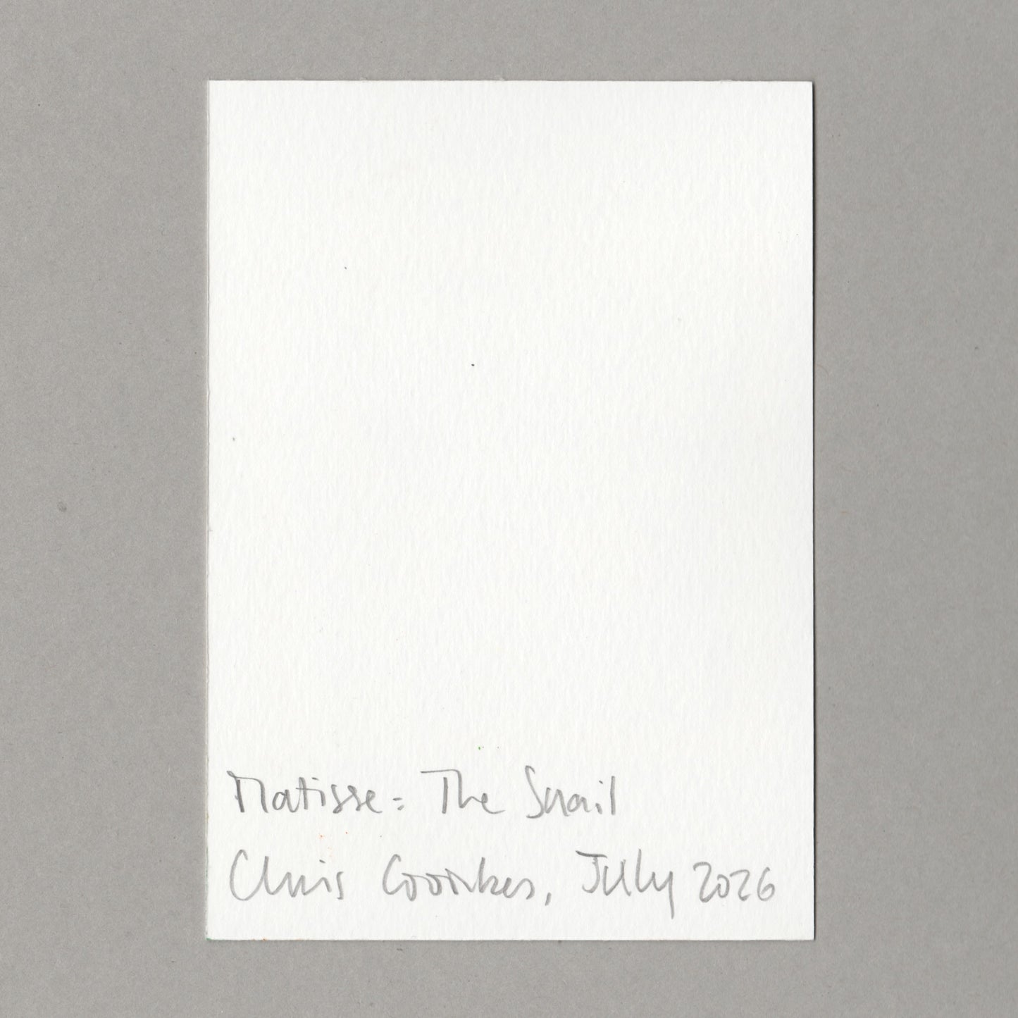 A white rectangular card with handwritten text at the bottom reading 'Matisse: The Snail Chris Coombes, July 2026', photographed against a plain grey background.