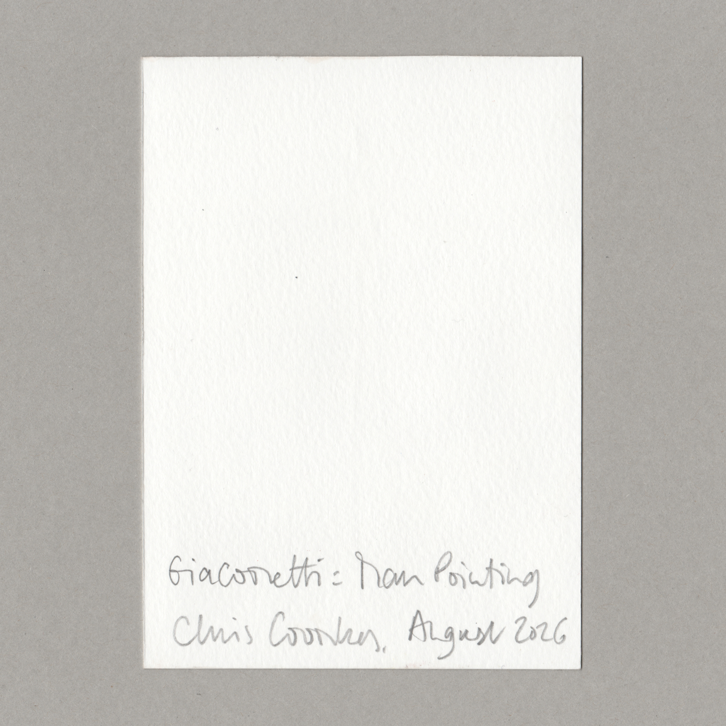 A small white rectangular paper card with handwritten text at the bottom reading 'Giacometti - Man Pointing Chris Coombes, August 2026', photographed against a plain grey background.