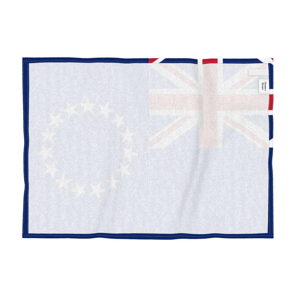 Reverse side of a tea towel with the flag of the Cook Islands. featuring a blue field with the Union Jack in the upper left and a circle of thirteen white stars on the right, shown flat against a white background.
