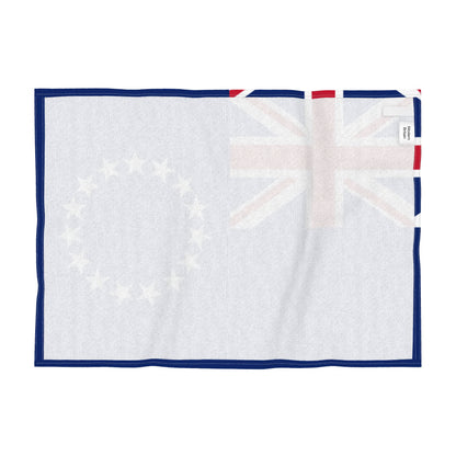 Reverse side of a tea towel with the flag of the Cook Islands. featuring a blue field with the Union Jack in the upper left and a circle of thirteen white stars on the right, shown flat against a white background.