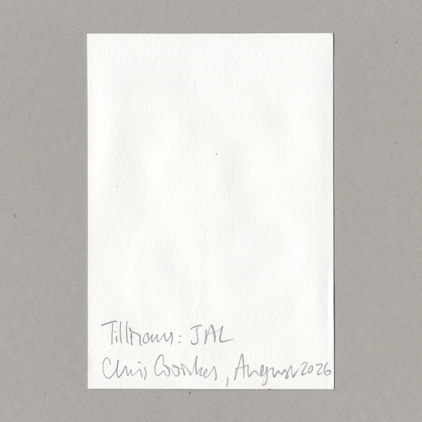 A blank white rectangular card or note with handwritten text at the bottom reading 'Tillmans: JAL Chris Coombes , August 2026', photographed against a plain gray background.